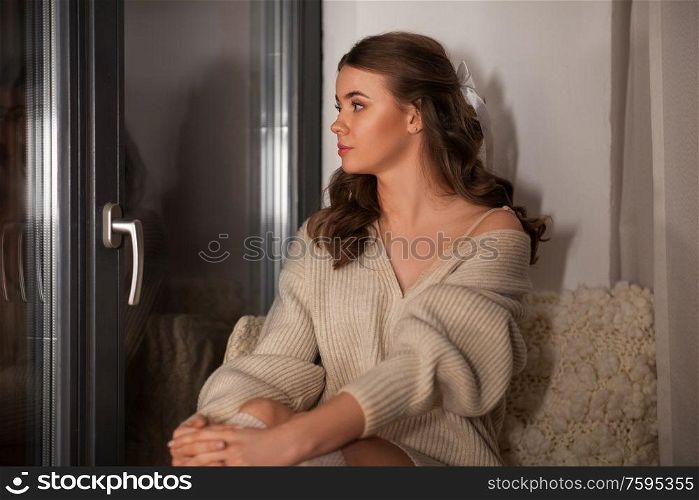 winter, comfort and people concept - young woman in pullover sitting at window at home. woman in pullover sitting at window at home