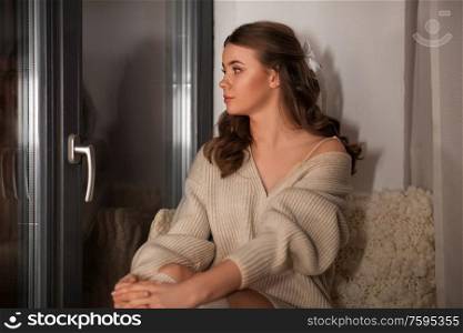 winter, comfort and people concept - young woman in pullover sitting at window at home. woman in pullover sitting at window at home