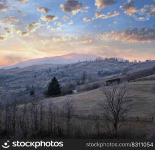 Winter coming. Last good weather days in autumn mountains countryside morning peaceful picturesque scene. Dirty road from hills to the village.