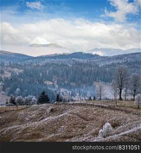 Winter coming. Picturesque foggy and moody morning scene in late autumn mountain countryside with hoarfrost on grasses, trees, slopes. Ukraine, Carpathian Mountains.