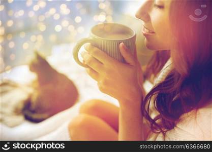 winter, cosiness, leisure and people concept - close up of happy young woman with cup of coffee or cacao and cat in bed at home. close up of happy woman with cup of cocoa at home