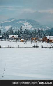 Winter countryside mountain landscape with wooden houses covered with snow, forests in the misty distant backdrop. Picturesque and peaceful wintry scene European resort location Copy space for text