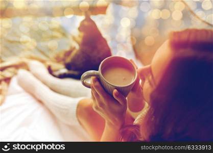 winter, coziness, leisure and people concept - close up of happy young woman with cup of coffee or cacao and cat in bed at home. close up of happy woman with cocoa cup at home