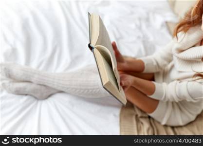 winter, coziness, leisure and people concept - close up of young woman reading book in bed at home