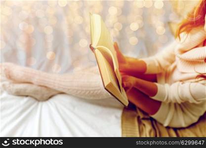 winter, coziness, leisure and people concept - close up of young woman reading book in bed at home. close up of young woman reading book in bed