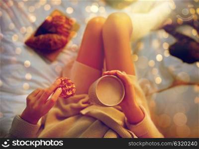 winter, coziness, leisure and people concept - close up of young woman with cup of coffee or cacao and cookie in bed at home. close up of woman with cocoa cup and cookie in bed