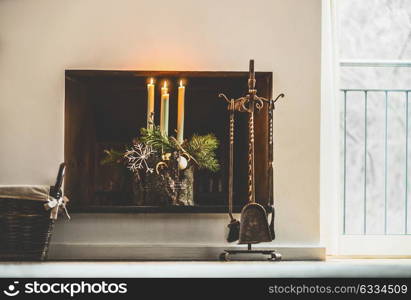 Winter cozy home decoration and festive holiday atmosphere with burning candles, fir branches and snowflakes at fireplace in living room at window. Decorated Fourth Advent wreath