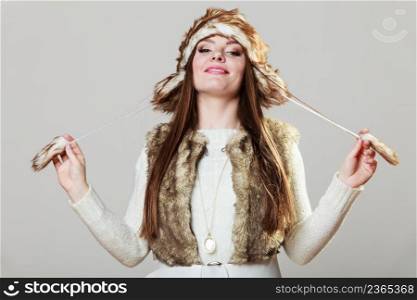 Winter cute girl fashion. Smiling woman wearing sweater fur vest and warm hat in freezing cold time playing with cap.. Winter time girl fashion.
