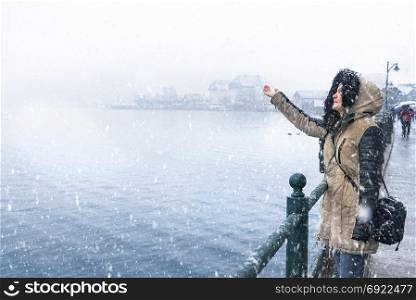 Winter destinations theme image with a woman standing on the Hallstatter lakeshore, catching snowflakes and enjoying the snowfall, in Hallstatt town, Austria.