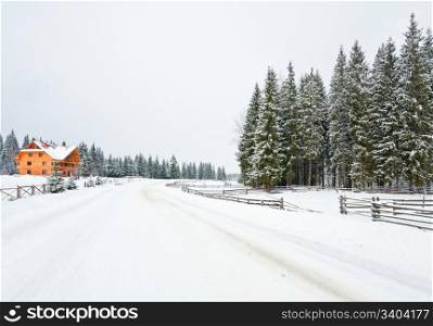 winter dull mountain landscape with fence , wooden house and country road