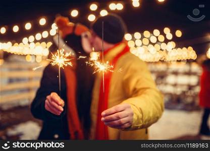 Winter evening, love couple with sparklers kissing outdoors. Man and woman having romantic meeting on city street with lights