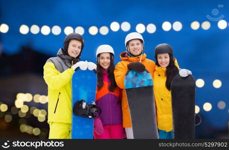 winter, extreme sport and people concept - happy friends in helmets with snowboards outdoors over christmas lights background. happy friends in helmets with snowboards