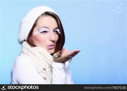 winter fashion beautiful woman in warm clothing stylish creative make up false long white eye lashes blowing a kiss blue background