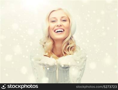 winter, fashion, christmas and people concept - smiling young woman in earmuffs and sweater holding something on her empty palms. woman in winter earmuffs showing empty palms