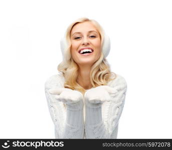 winter, fashion, christmas and people concept - smiling young woman in earmuffs and sweater holding something on her empty palms