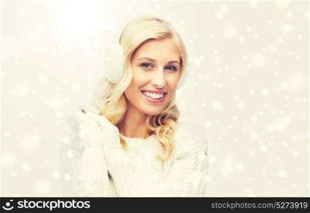 winter, fashion, christmas and people concept - smiling young woman in earmuffs and sweater. smiling young woman in winter earmuffs and sweater