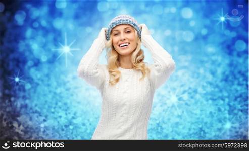 winter, fashion, christmas and people concept - smiling young woman in hat, sweater and gloves over blue glitter or lights background