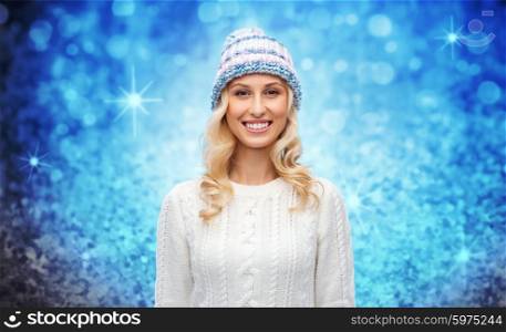 winter, fashion, christmas and people concept - smiling young woman in hat and sweater over blue glitter or lights background