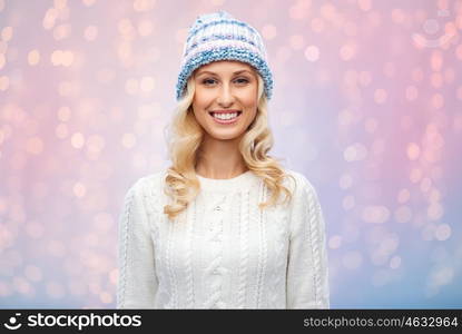 winter, fashion, christmas and people concept - smiling young woman in winter hat, sweater and gloves over rose quartz and serenity lights background