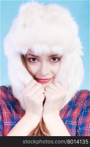 Winter fashion. Close up young woman wearing fashionable wintertime clothes white fur cap studio shot on blue background