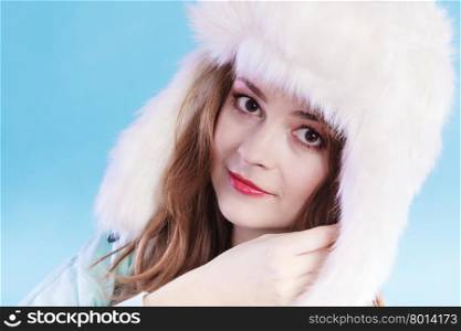 Winter fashion. Close up young woman wearing fashionable wintertime clothes white fur cap studio shot on blue background
