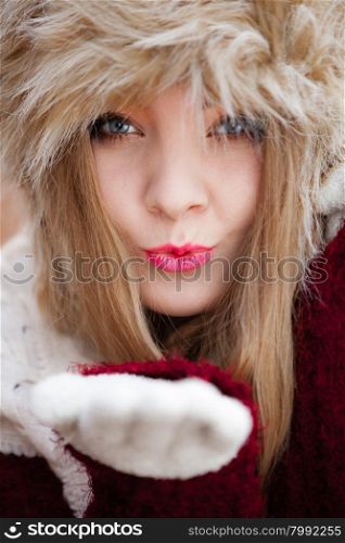 Winter fashion. Closeup young woman wearing fashionable wintertime clothes fur cap blowing a kiss outdoor portrait