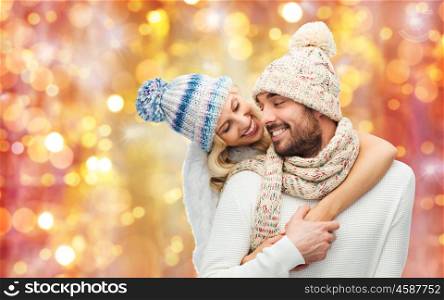 winter, fashion, couple, christmas and people concept - smiling man and woman in hats and scarf hugging over lights background