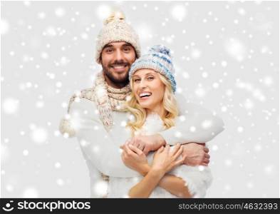 winter, fashion, couple, christmas and people concept - smiling man and woman in hats and scarf hugging over snow background