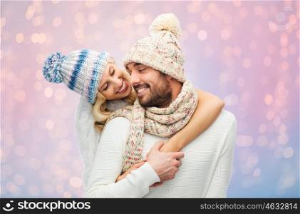 winter, fashion, couple, christmas and people concept - smiling man and woman in hats and scarf hugging over rose quartz and serenity lights background