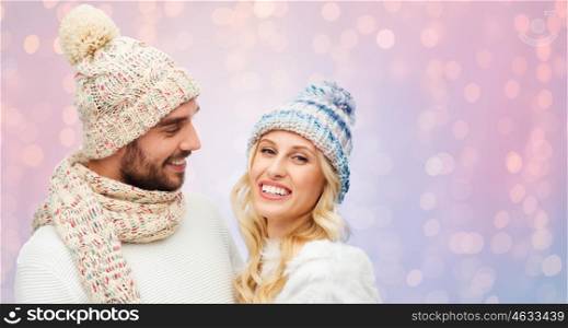 winter, fashion, couple, christmas and people concept - smiling man and woman in hats and scarf over rose quartz and serenity lights background