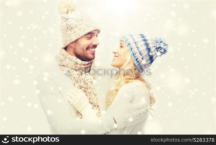 winter, fashion, couple, christmas and people concept - smiling man and woman in hats and scarf hugging. smiling couple in winter clothes hugging