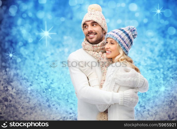 winter, fashion, couple, christmas and people concept - smiling man and woman in hats and scarf hugging over blue glitter or lights background