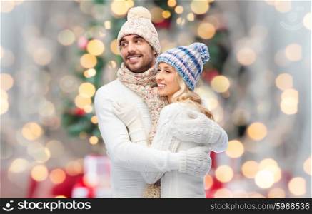 winter, fashion, couple, christmas and people concept - smiling man and woman in hats and scarf hugging over lights background