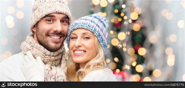winter, fashion, couple, christmas and people concept - smiling man and woman in hats and scarf hugging over holidays lights background