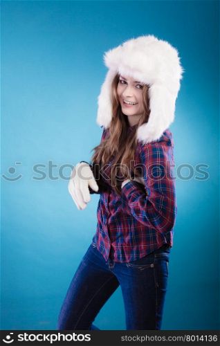 Winter fashion. Funny young woman teen girl wearing plaid shirt and fashionable wintertime clothes white fur cap goofing studio shot on blue background