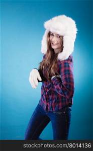 Winter fashion. Funny young woman teen girl wearing plaid shirt and fashionable wintertime clothes white fur cap goofing studio shot on blue background