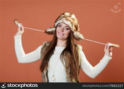 Winter fashion. Happy young woman wearing fashionable wintertime clothes fur cap on orange background