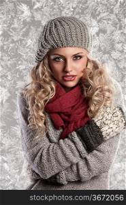 winter fashion shot of a beautiful girl with long curled blonde hair wearing a grey woolen cap, a grey sweater and warm gloves