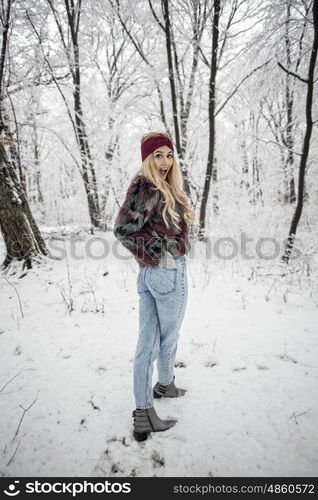 Winter fashion woman posing in the snowy forest wearing a warm fur jacket