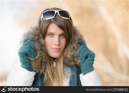 Winter fashion - woman with fur hood and sunglasses outside, desaturated colors