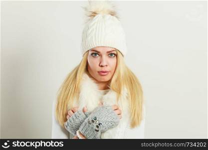 Winter fashion. Young blonde woman wearing fashionable wintertime clothes white fur scarf, woolen cap and gloves, studio shot. Woman wearing warm winter clothing