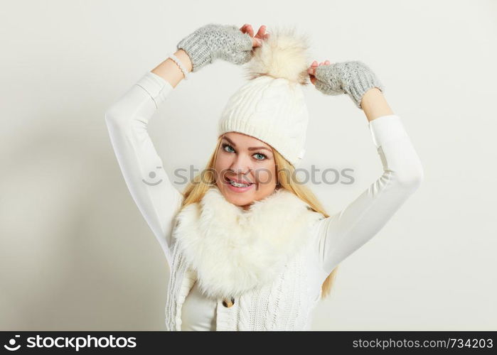 Winter fashion. Young blonde woman wearing fashionable wintertime clothes white fur scarf, woolen cap and gloves, studio shot. Woman wearing warm winter clothing