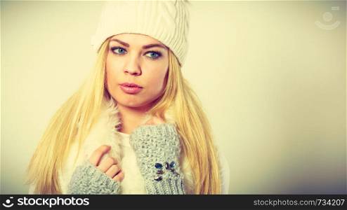 Winter fashion. Young blonde woman wearing fashionable wintertime clothes white fur scarf, woolen cap and gloves, studio shot. Woman wearing warm winter clothing
