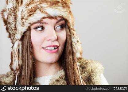 Winter female fashion. Portrait of beautiful young lady in fur cap on grey background in studio.