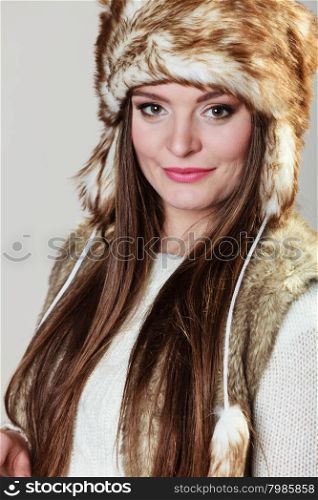 Winter female fashion. Portrait of beautiful young lady in fur cap on grey background in studio.