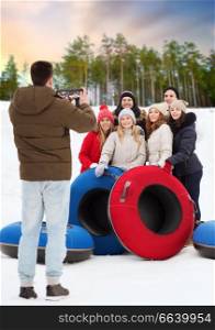 winter, friendship and technology concept - group of happy teenage friends with snow tubes taking photo by tablet pc computer over natural background. friends with snow tubes taking photo by tablet pc