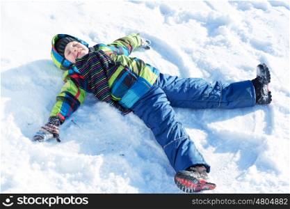 Winter fun. Happy kid lies on snow in winter park