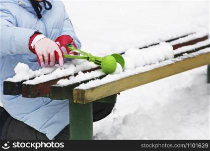 Winter games. Image of a child sitting in the snow near an old bench and sculpting snowballs.