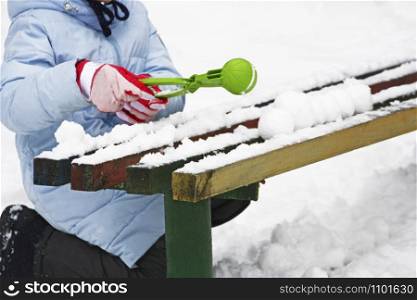 Winter games. Image of a child sitting in the snow near an old bench and sculpting snowballs.