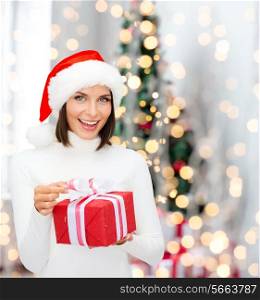 winter, happiness, holidays and people concept - smiling woman in santa helper hat with gift box over living room with christmas tree background